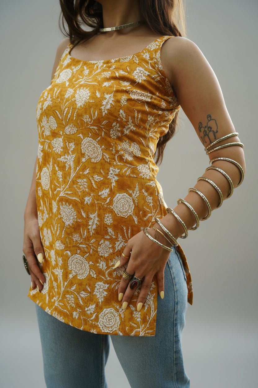 Close-up of a sleeveless mustard yellow kurti featuring intricate white floral block print, a soft curved neckline, and side slits for ease. The kurti is styled with denim, highlighting its tailored fit and breezy cotton fabric ideal for summer wear.