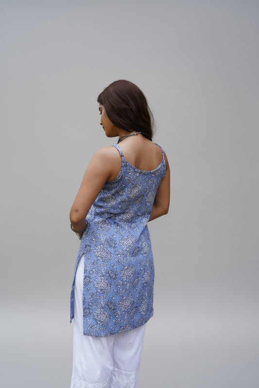 Back view of a sleeveless periwinkle blue kurti with white and black floral block prints and subtle vertical stripes. The kurti features a scoop back and side slits, paired with white palazzo pants for a light and airy ethnic ensemble.