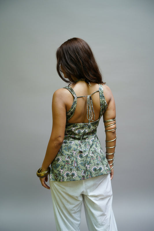 Back view of a sage green kurti featuring floral and bird motifs, designed with a square-cut open back and adjustable tie-up detailing. The fitted silhouette and sleeveless cut are paired with white palazzo pants for a refined and breezy ethnic look.
