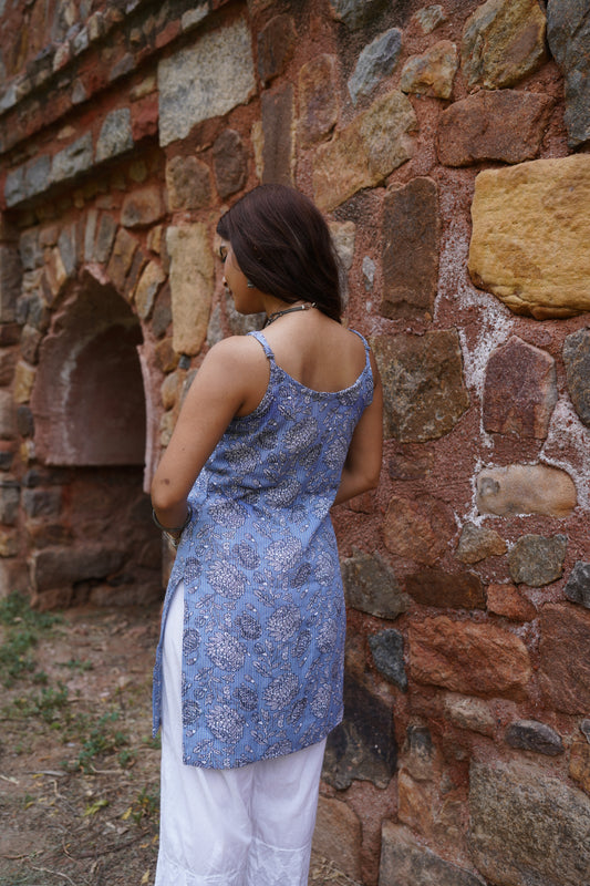 Back view of a sleeveless periwinkle blue kurti with white and black floral block prints and subtle vertical stripes. The kurti features a scoop back and side slits, paired with white palazzo pants for a light and airy ethnic ensemble.