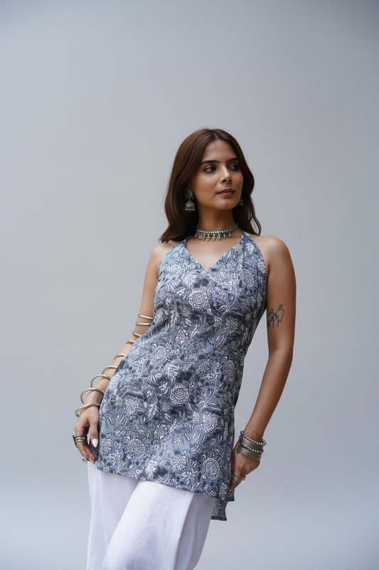 Sleeveless grey halter-neck kurti with intricate white floral block prints and a subtle sweetheart neckline. The kurti features a tailored fit with side slits and is paired with white palazzo pants, offering a graceful blend of tradition and contemporary style.