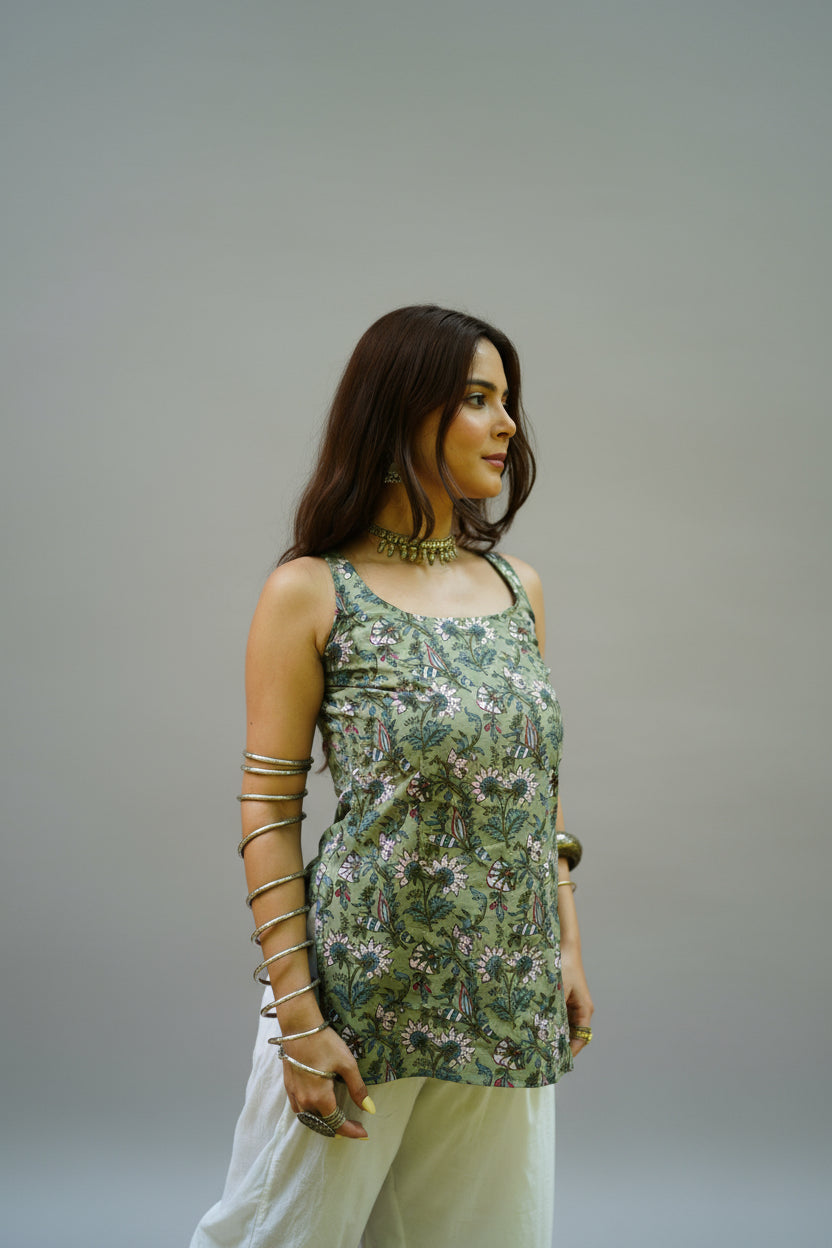 Sleeveless sage green kurti adorned with detailed floral and bird motifs in soft pink, white, and indigo shades. Featuring a square neckline and relaxed fit, the kurti is paired with white palazzo pants, creating a breezy and artistic ethnic look