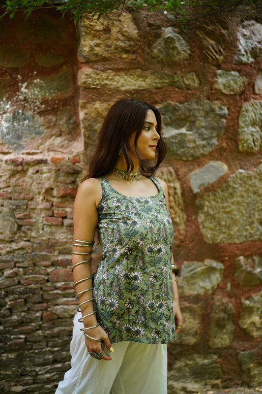 Sleeveless sage green kurti adorned with detailed floral and bird motifs in soft pink, white, and indigo shades. Featuring a square neckline and relaxed fit, the kurti is paired with white palazzo pants, creating a breezy and artistic ethnic look